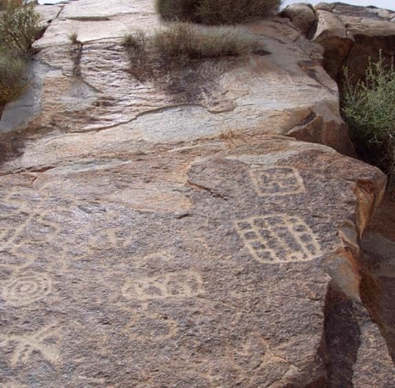 Ancient petroglyphs carved into a large rock surface with geometric patterns and spiral shapes.